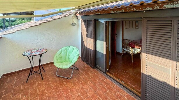 A balcony with a tiled floor, a green chair, and a small table. - Villa Carra - Ansedonia (Ansedonia)