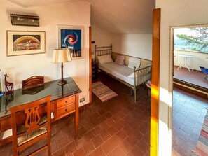 Ein Schlafzimmer mit einem Bett, einem Schreibtisch und einem Stuhl. Ein Fenster bietet einen Ausblick nach draußen.