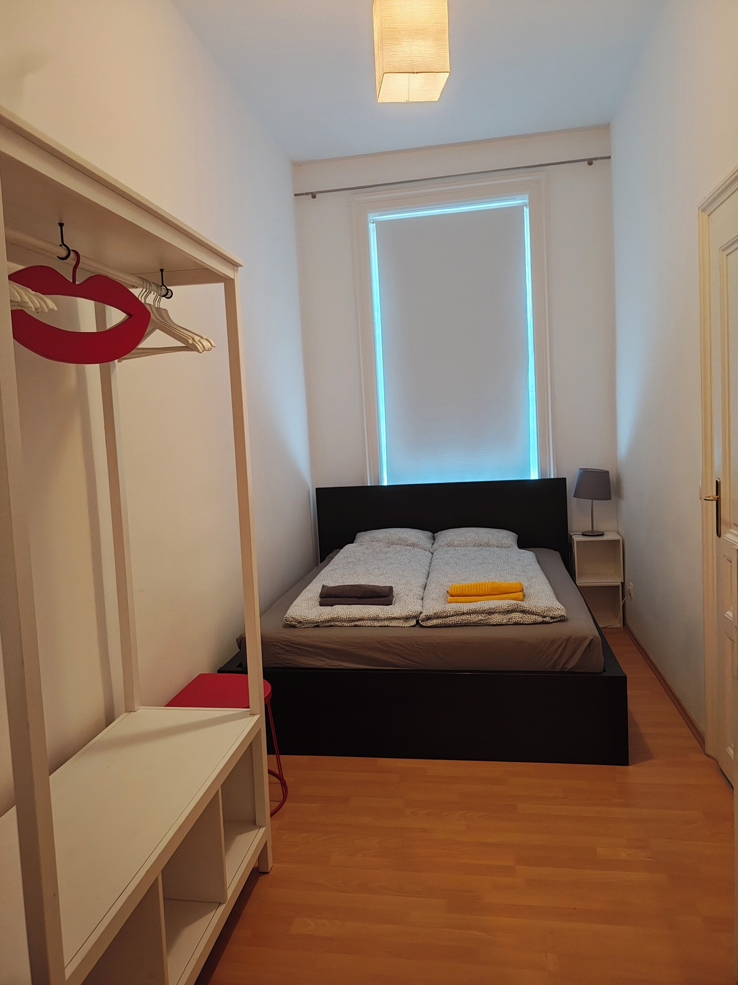 A bedroom with a bed, a wardrobe, a bedside table, and a lamp.