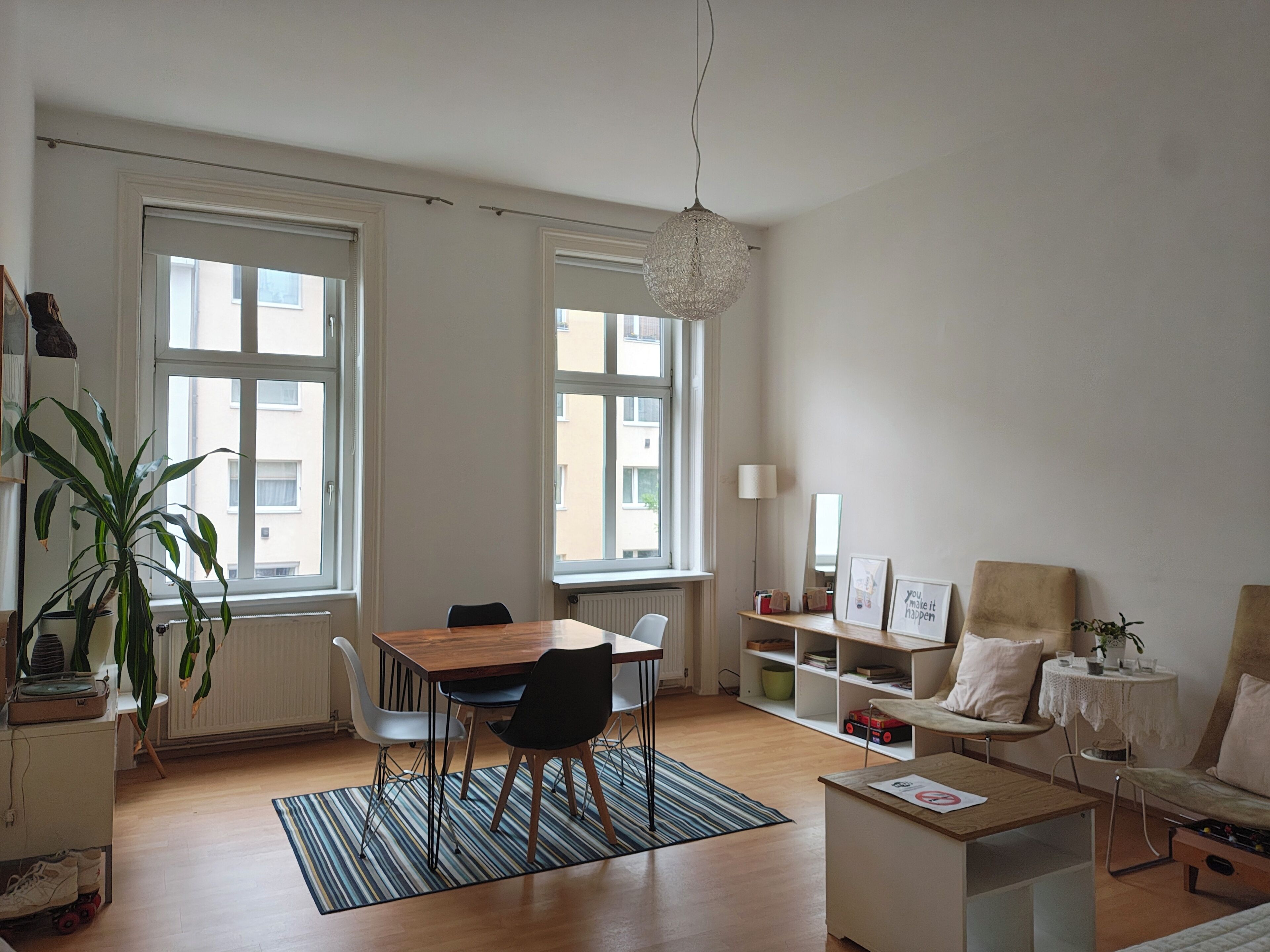 Ein modernes Wohnzimmer mit Essbereich, großen Fenstern, einer Pendelleuchte und einem Bücherregal.