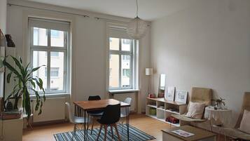 Ein modernes Wohnzimmer mit Essbereich, großen Fenstern, einer Pendelleuchte und einem Bücherregal.