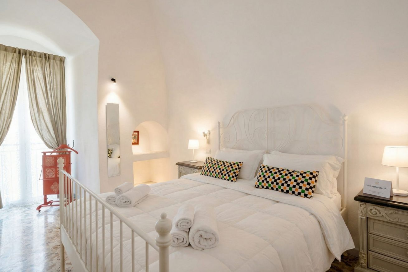 Un letto rifatto con asciugamani arrotolati, un comodino con una lampada e un carrello rosso in una camera d'albergo.