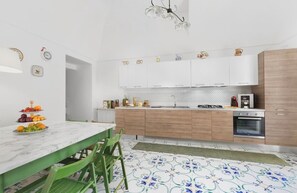 A modern kitchen with white cabinets, a marble countertop, and a green dining table.