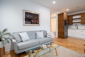 A modern living room with a grey sofa, a glass coffee table, and a framed artwork above. - Sustainable Garden Suite Retreat - Modern, serene & peaceful oasis (Nanaimo)