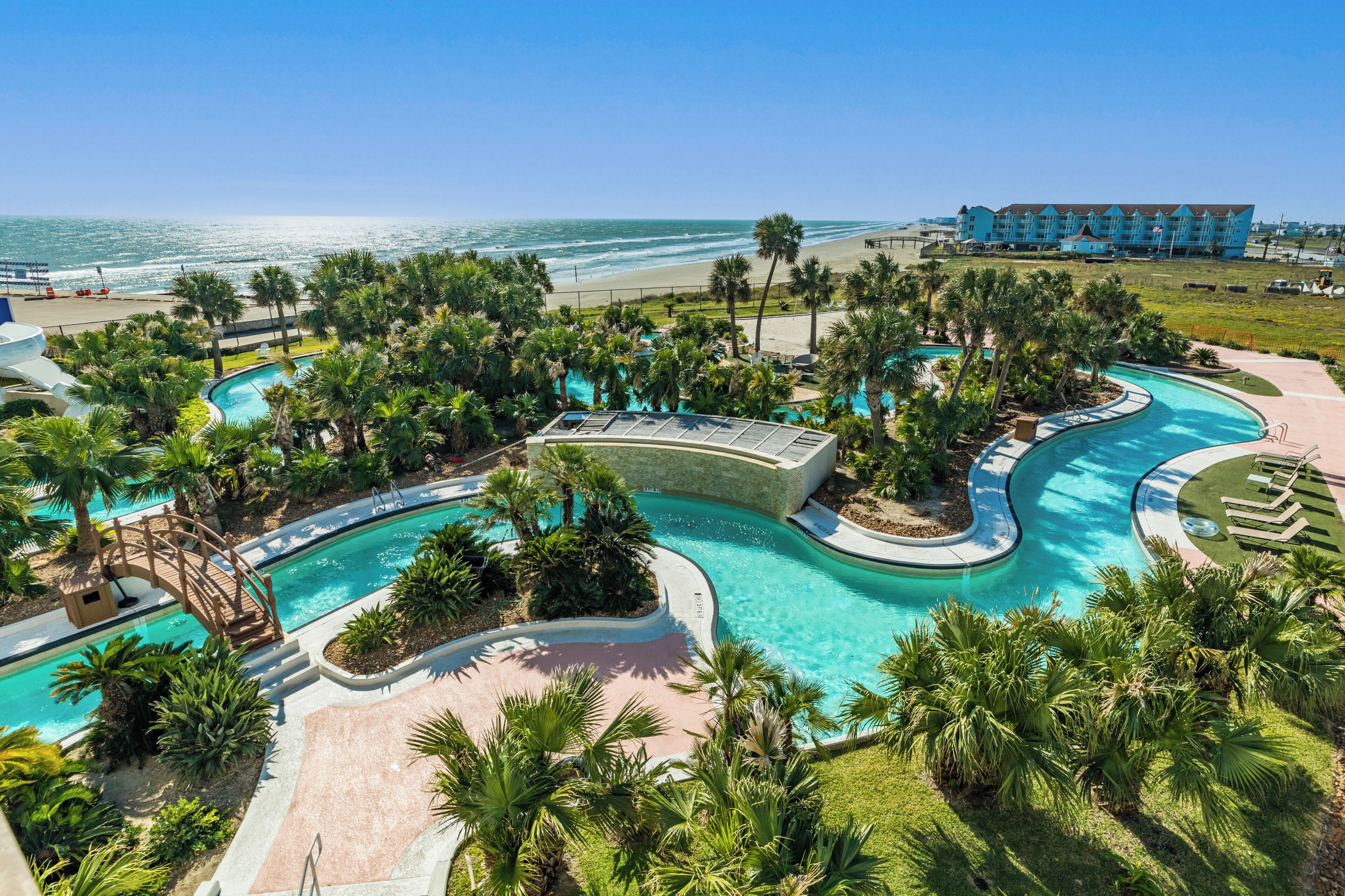 A resort with a large pool area, palm trees, and a view of the ocean.