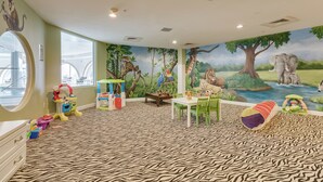 Een kinderspeelkamer met een tapijt met zebraprint, een muurschildering van een jungle en diverse speelmeubels.
