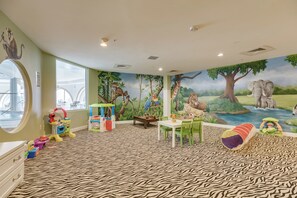 Ein Spielzimmer für Kinder mit einem zebra-gemusterten Teppich, einer Wandmalerei einer Dschungel-Szene und verschiedenen Spielmöbeln.