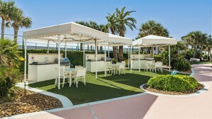 Een terras buiten met witte parasols, een barbecuehoek en zitplaatsen.