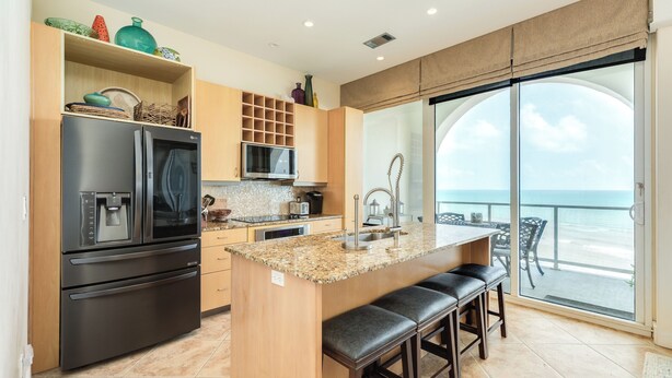 Een moderne keuken met een groot eiland, roestvrijstalen apparatuur en uitzicht op de oceaan door een schuifdeur van glas.