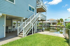 Une propriété située au bord de l’eau, dotée d’un espace extérieur couvert avec des sièges, d’un escalier menant à une terrasse et d’un canal en arrière-plan.