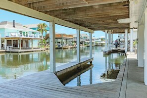 A waterfront property with a covered dock area, wooden deck, and multiple buildings with balconies. - Pet Friendly Canal Home w/ Top Level Viewing Deck,  Boat Slip & More! (Galveston)