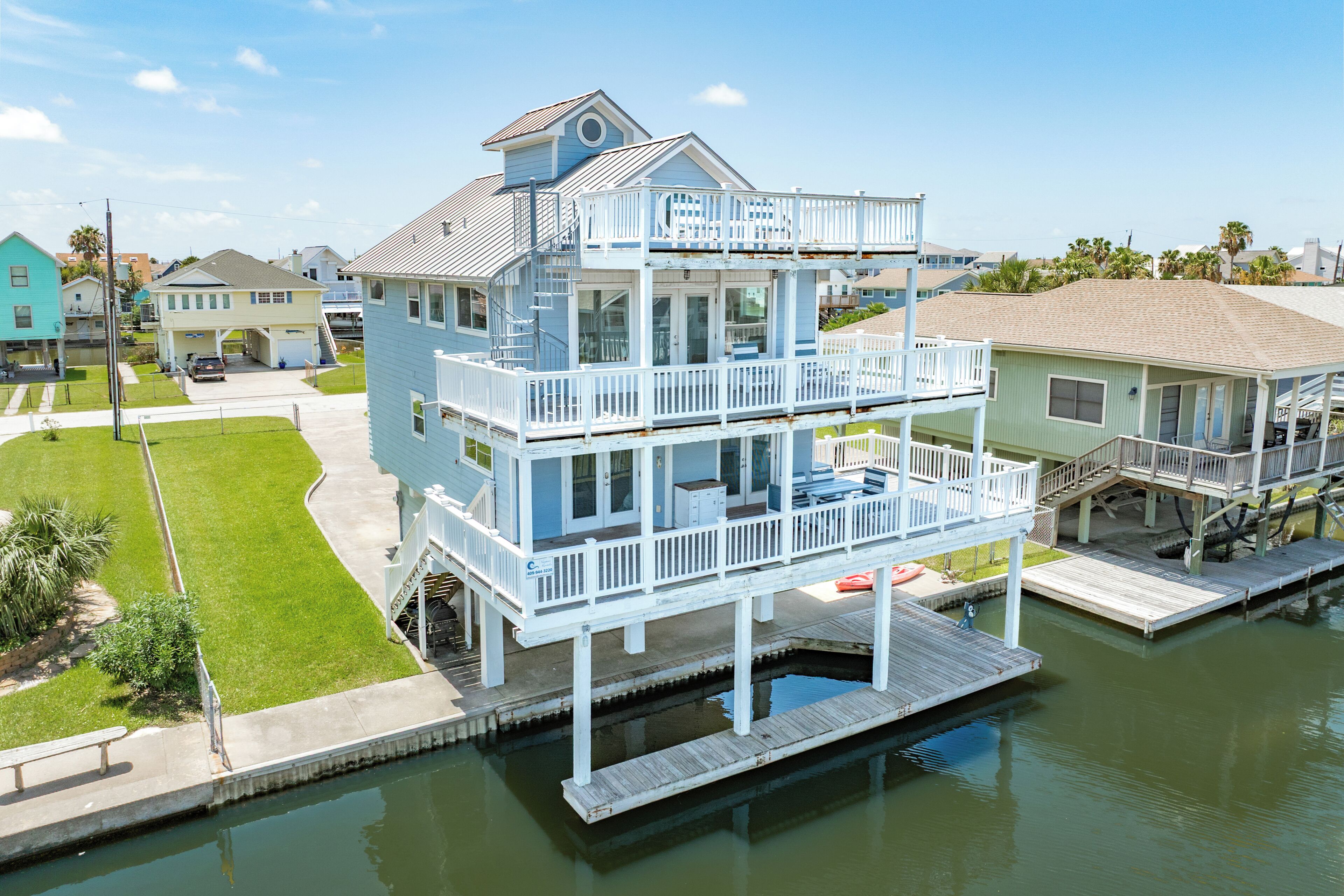A multi-story waterfront property with balconies, a dock, and a small boat.