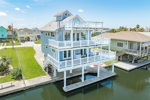 A multi-story waterfront property with balconies, a dock, and a small boat. - Pet Friendly Canal Home w/ Top Level Viewing Deck,  Boat Slip & More! (Galveston)