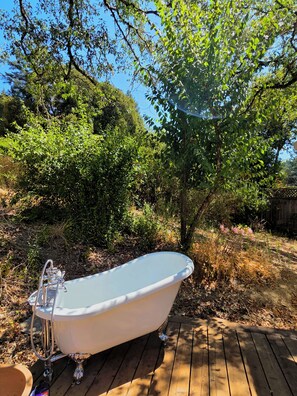 A freestanding bathtub on a wooden deck surrounded by dense greenery.
