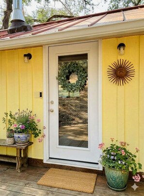 A yellow building with a white door, a wreath, and potted plants. - Sunshine Cabin - Peaceful Retreat in The Redwoods (Garberville)