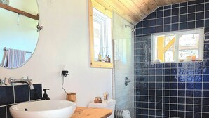 A bathroom with a wooden vanity, a round mirror, a white sink, a toilet, and a shower area with black tiles.