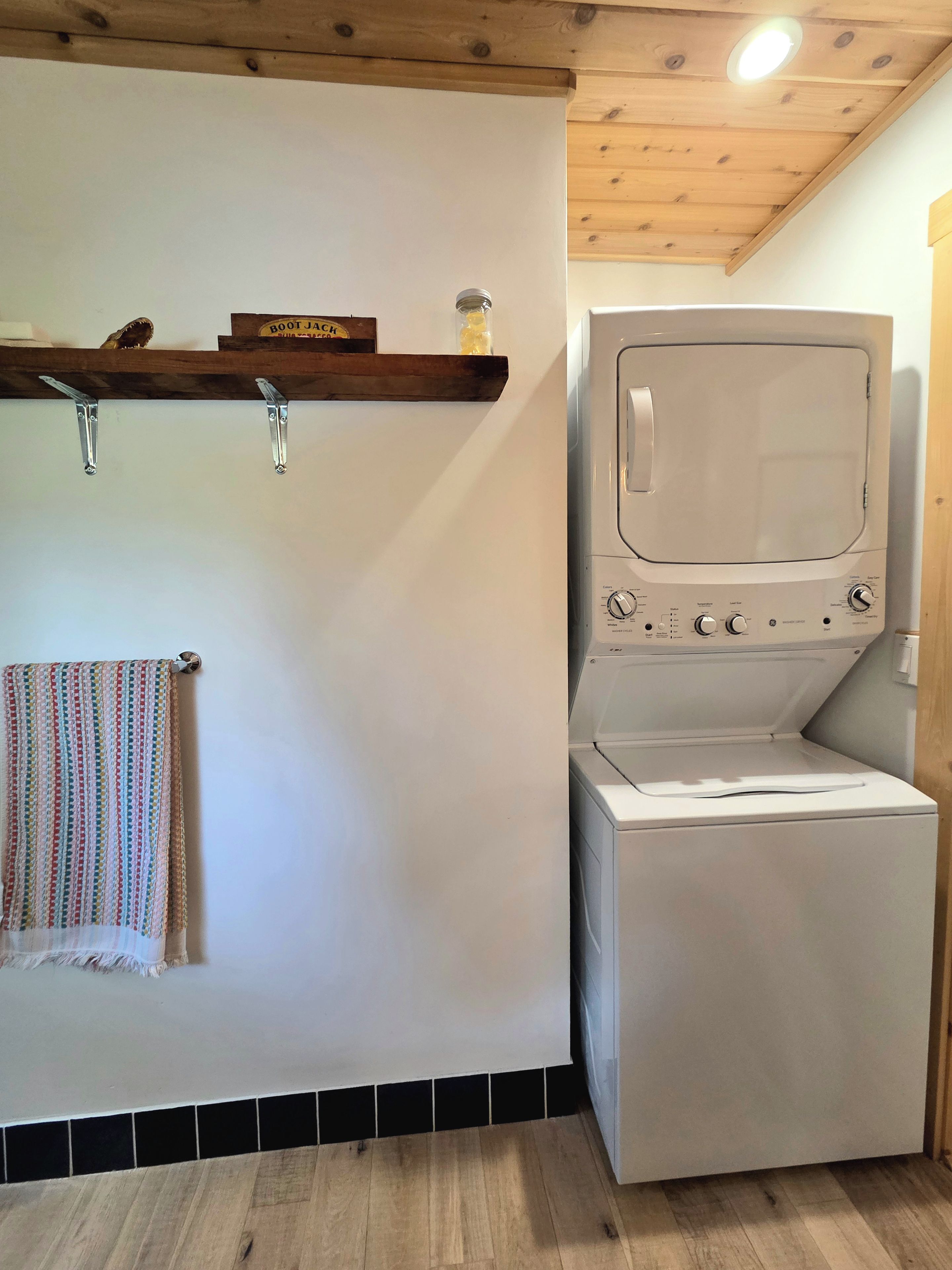 A laundry area with a washing machine and dryer, a wooden shelf with items, and a towel rack.