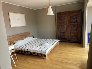 Ein Schlafzimmer mit einem hölzernen Bett, einem Holzschrank, einem weißen Nachttisch und einer Pendelleuchte.