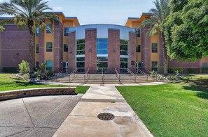 A multi-story building with a central atrium, surrounded by a well-maintained lawn and palm trees. - Modern King Suite - Steps from UAT and near ASU (Tempe)