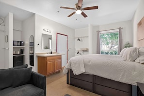 A bedroom with a bed, a ceiling fan, a window with curtains, a bedside table, and a chair. - Modern King Suite - Steps from UAT and near ASU (Tempe)