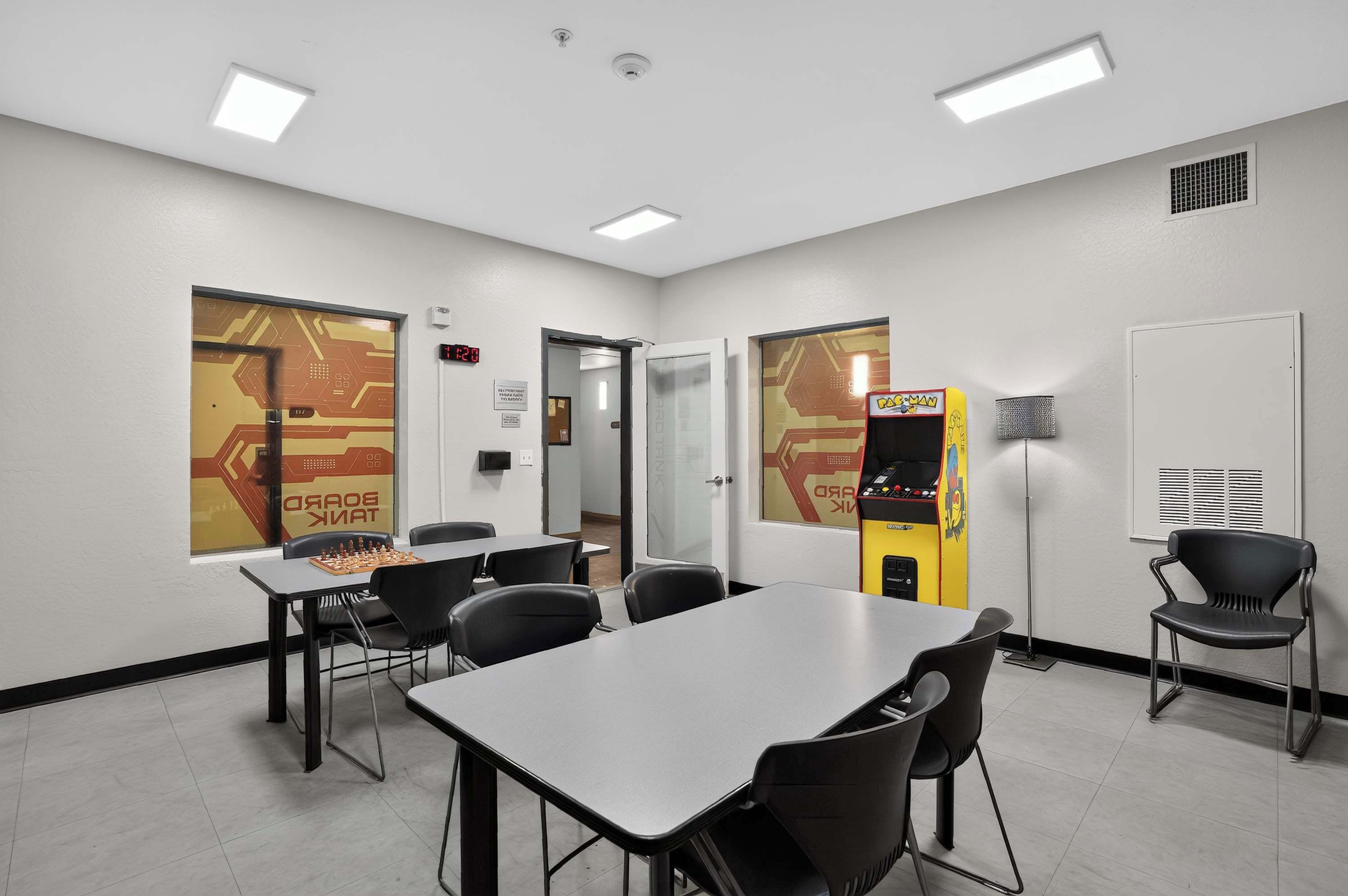 A conference room with a chessboard, chairs, tables, a clock, and a vending machine.
