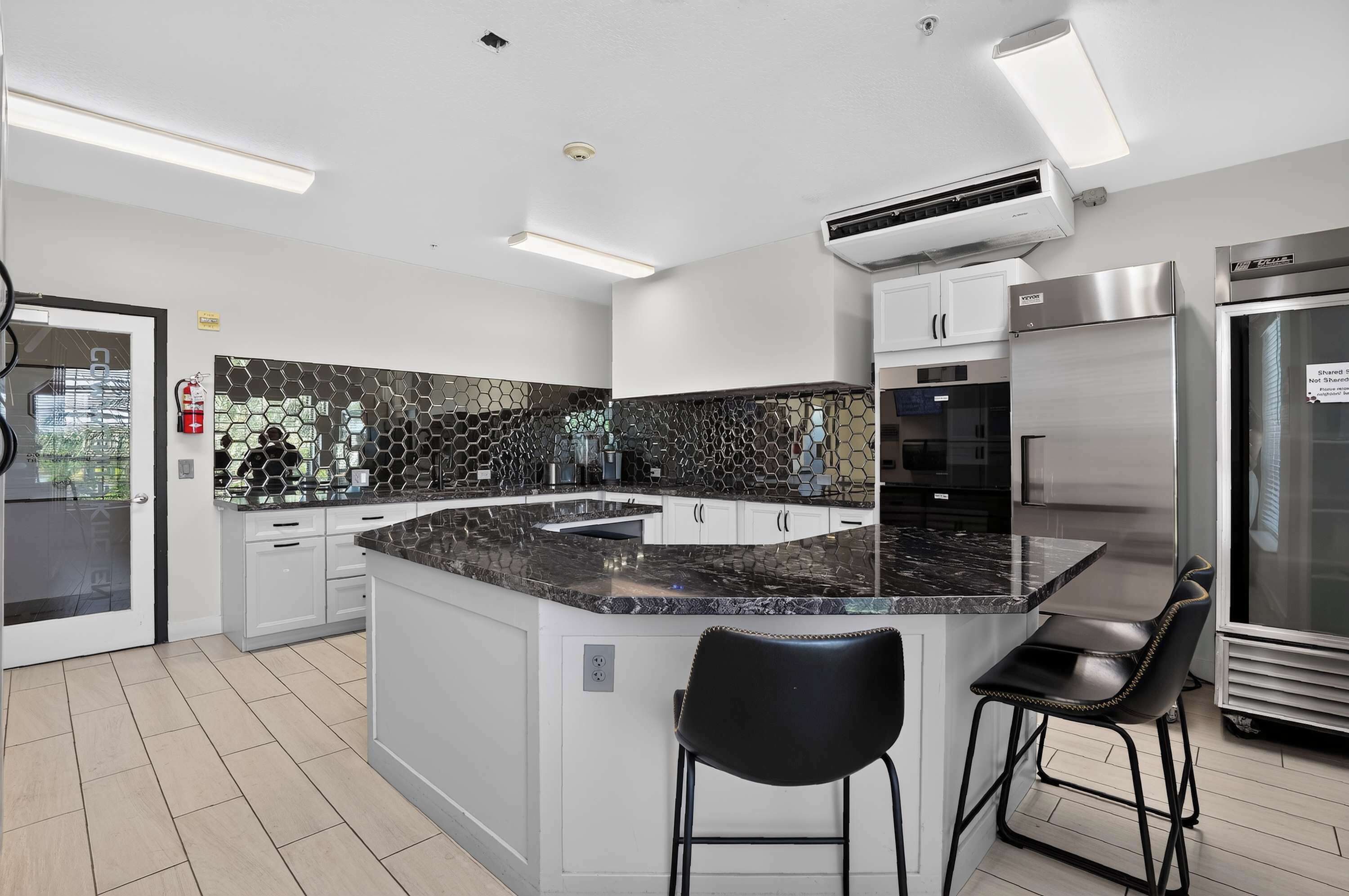 A modern kitchen with a central island, white cabinetry, a black hexagonal backsplash, stainless steel appliances, and a black bar stool.