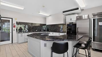 A modern kitchen with a central island, white cabinetry, a black hexagonal backsplash, stainless steel appliances, and a black bar stool.