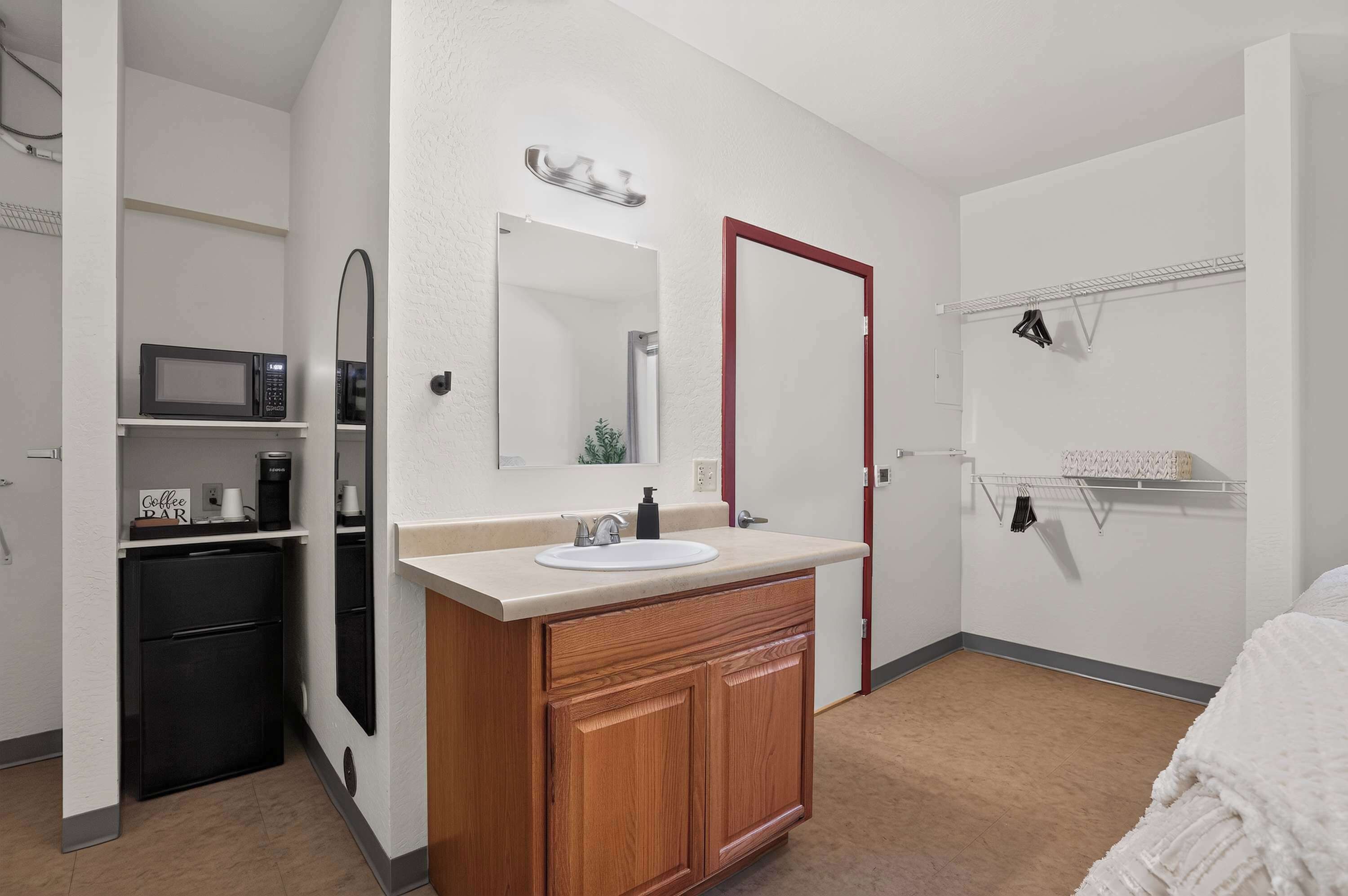 Une salle de bain moderne avec un meuble-lavabo en bois, un lavabo blanc, un miroir, une porte rouge et un espace douche.