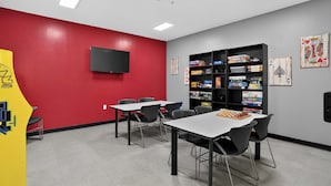 Ein Zimmer mit roter Wand, einem angebauten Flachbildfernseher, einem Bücherregal voller Brettspiele und einem Schachbrett auf einem Tisch.