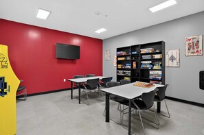 A room with a red wall, a flat-screen TV mounted on it, a bookshelf filled with board games, and a chessboard on a table. - Modern King Suite - Steps from UAT and near ASU (Tempe)