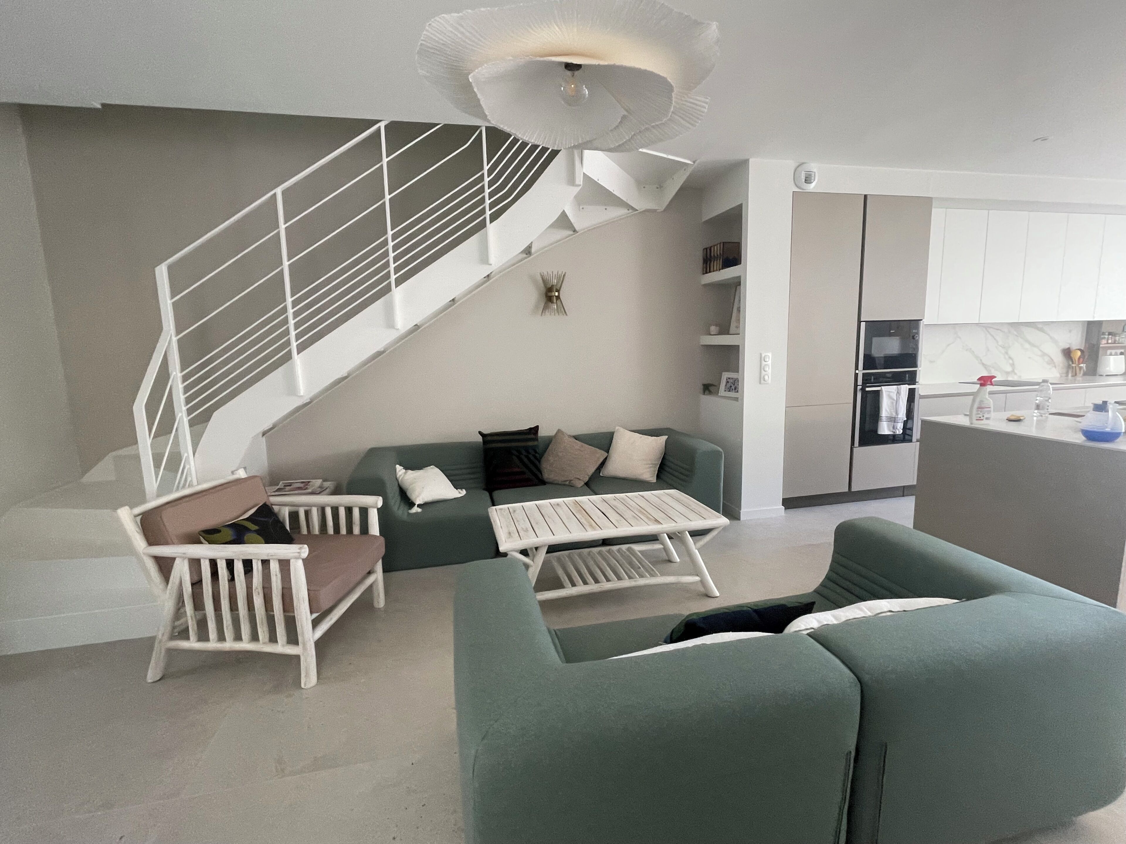 A modern living room with a staircase, a green sofa, a white coffee table, and a kitchen area.