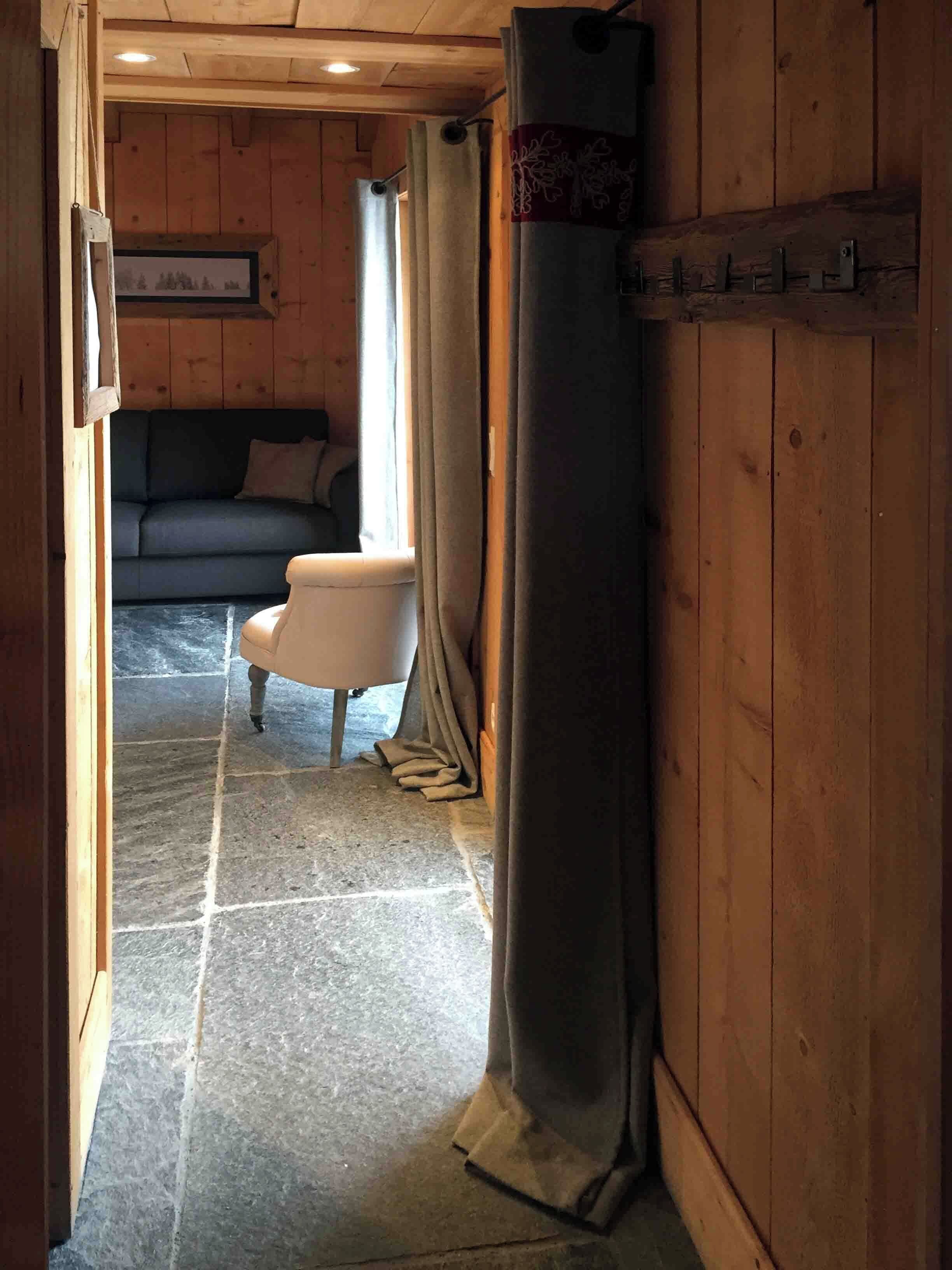 Un intérieur en bois avec un sol en pierre, un canapé, un fauteuil et un rideau.