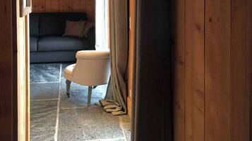 Un intérieur en bois avec un sol en pierre, un canapé, un fauteuil et un rideau.
