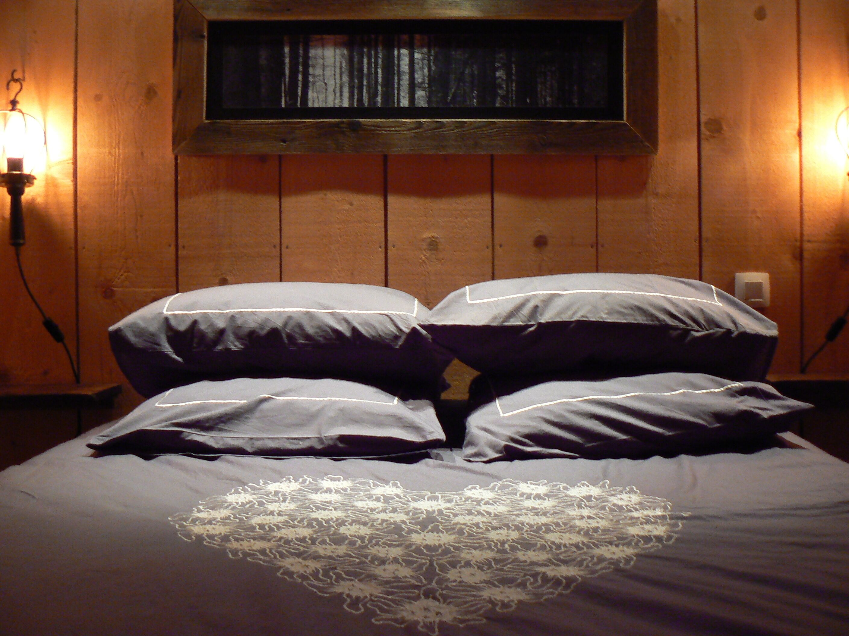 A bed with a heart-shaped lace design, wooden walls, and two wall-mounted lamps.