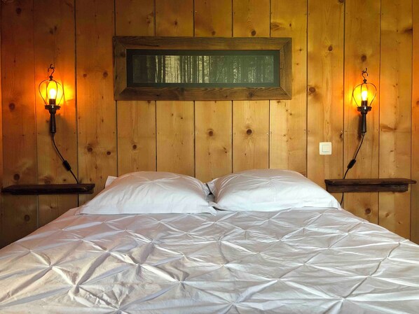 A bed with a white quilt in a wooden room with two wall-mounted lamps.