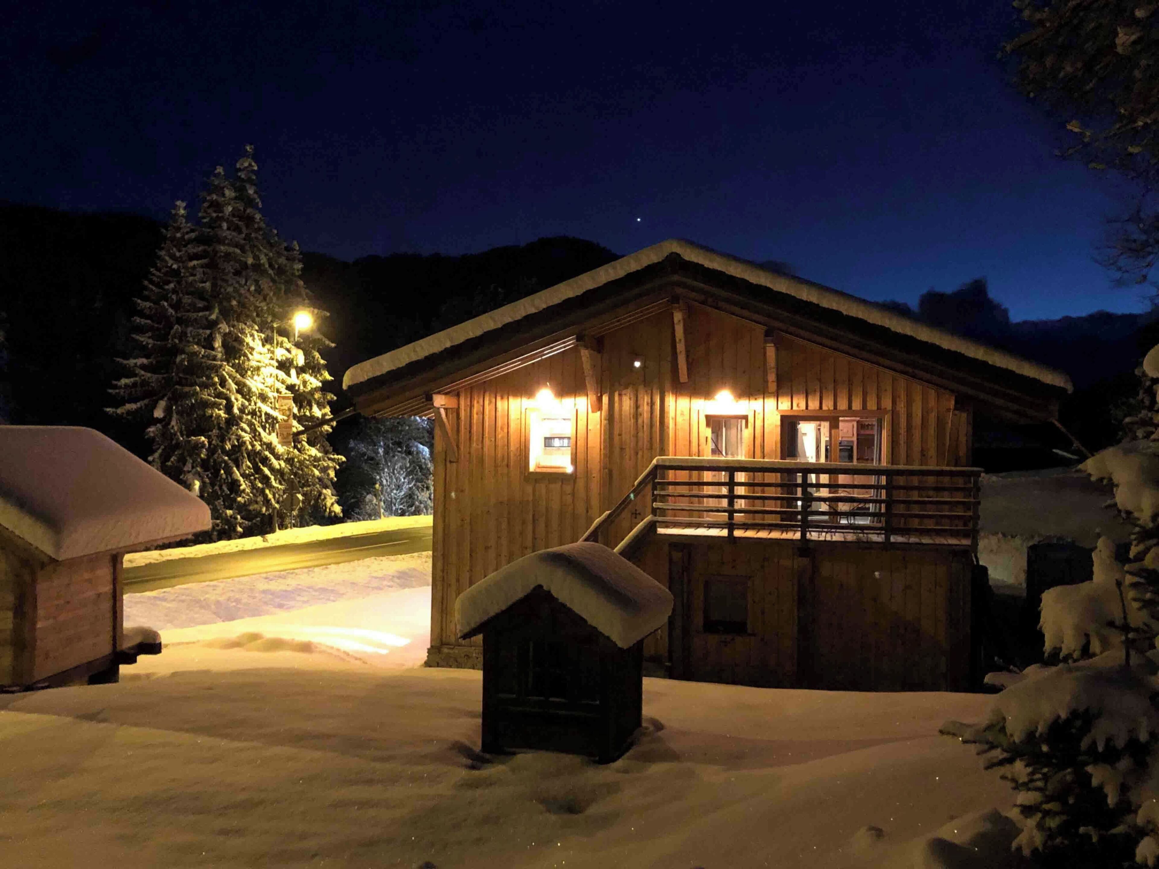 Een houten chalet met een balkon, omgeven door een besneeuwde omgeving en bomen.