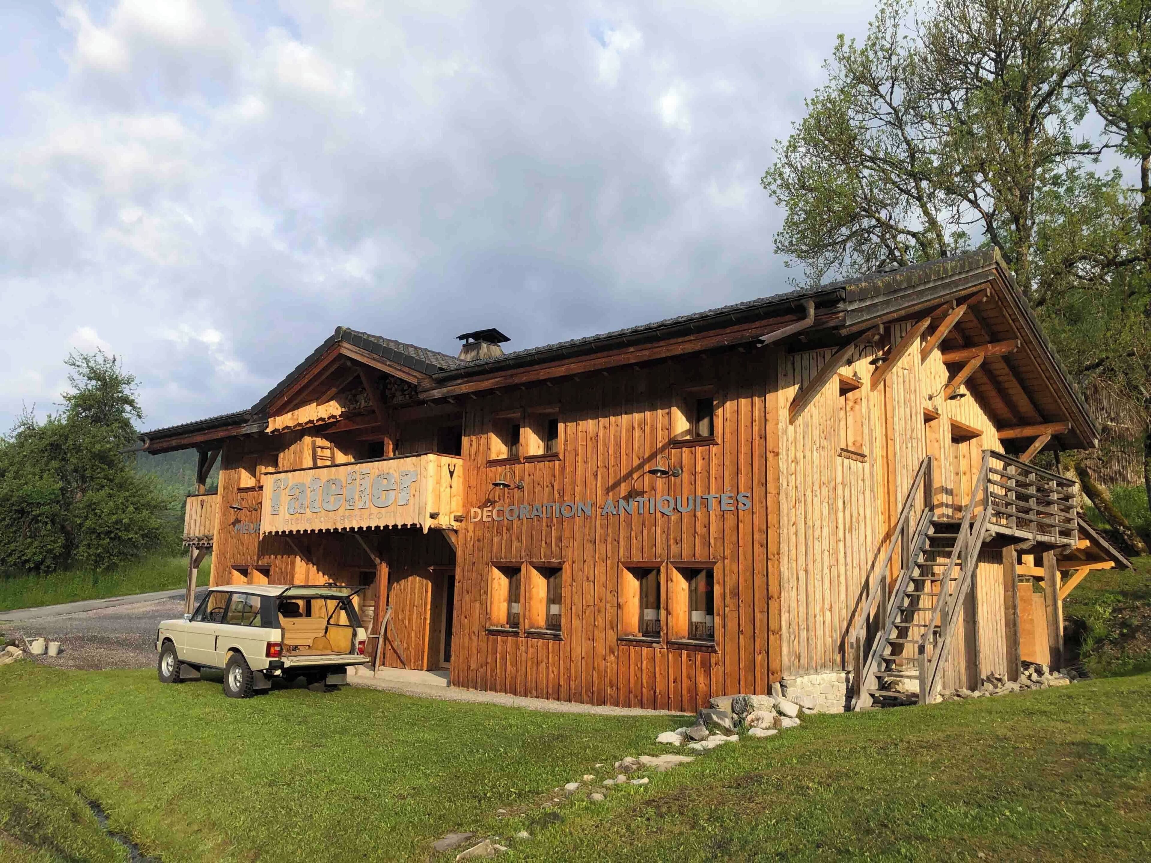 A wooden building with a sign reading 'DECORATION ANTIQUITES' and a vehicle parked in front.
