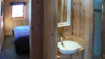Une chambre dans un chalet en bois, avec un lit, une salle de bain comprenant un lavabo et un miroir, et une fenêtre.