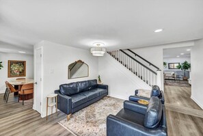 A modern living room with a sofa, a dining table, and a staircase.