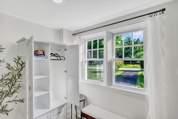 A white room with a large window, a wardrobe, and a small bench.