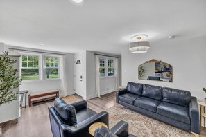 A living room with a black leather sofa, a coffee table, and a large window with curtains.