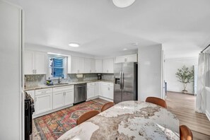 A modern kitchen with white cabinets, stainless steel appliances, and a dining area with a marble table.