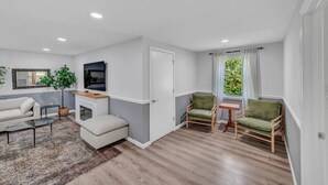 A modern living room with a sofa, a coffee table, a TV, and a small table with chairs. - Family Retreat with Pool & Playground (Roslyn)