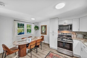 A modern kitchen with white cabinets, a built-in oven, a microwave, and a dining area with a round table and chairs.