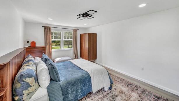 A bedroom with a bed, a wardrobe, a window with curtains, and a ceiling light fixture. - Family Retreat with Pool & Playground (Roslyn)