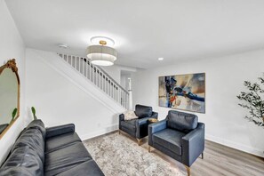 A modern living room with a staircase, a large abstract painting, and a mirror.
