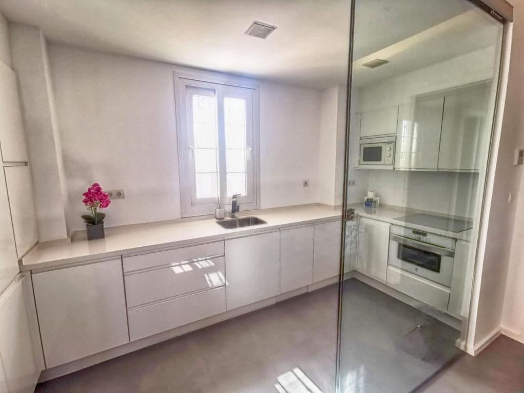 A modern kitchen with a glass partition, white cabinetry, and a window providing natural light.