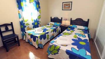 Een kamer met twee bedden, een stoel en een raam met gordijnen.