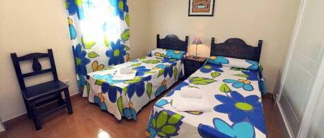 Habitación con dos camas, una silla y un ventanal con cortinas.