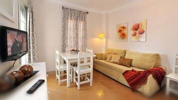 A living room with a TV, white furniture, a sofa, and a dining table.